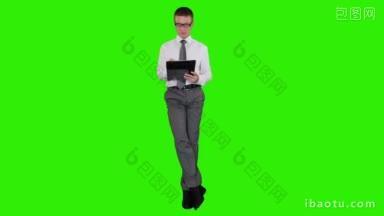 年轻的商人戴着眼镜，坐在绿色的屏幕上，在写字板上写字